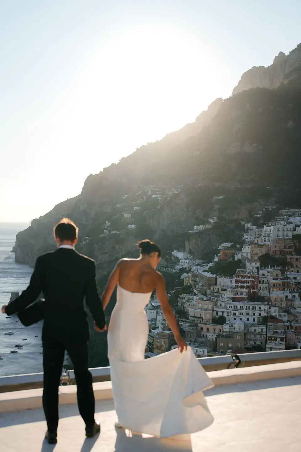 Bride and groom walking on the terrace of Villa Oliviero at sunset, Positano behind them.