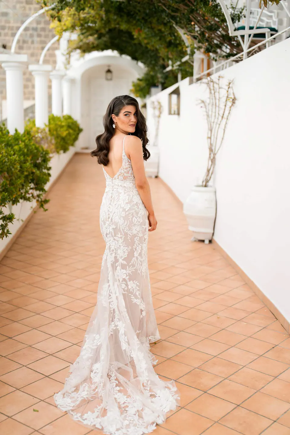 Bride walking along the white corridor of Villa Milù, flowing lace gown trailing softly behind.