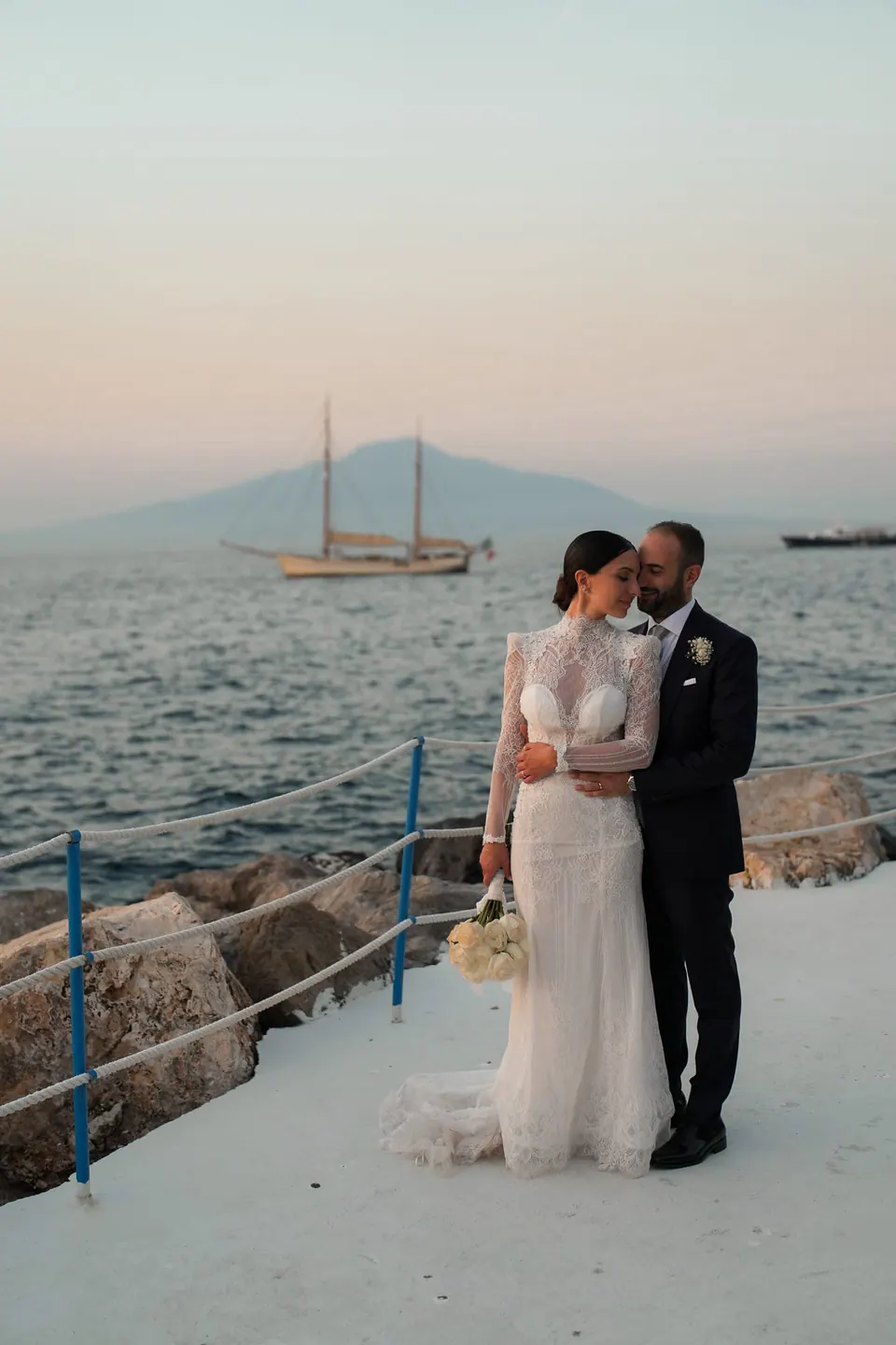 Bride and groom on the pier with a sailing boat and Vesuvius behind them