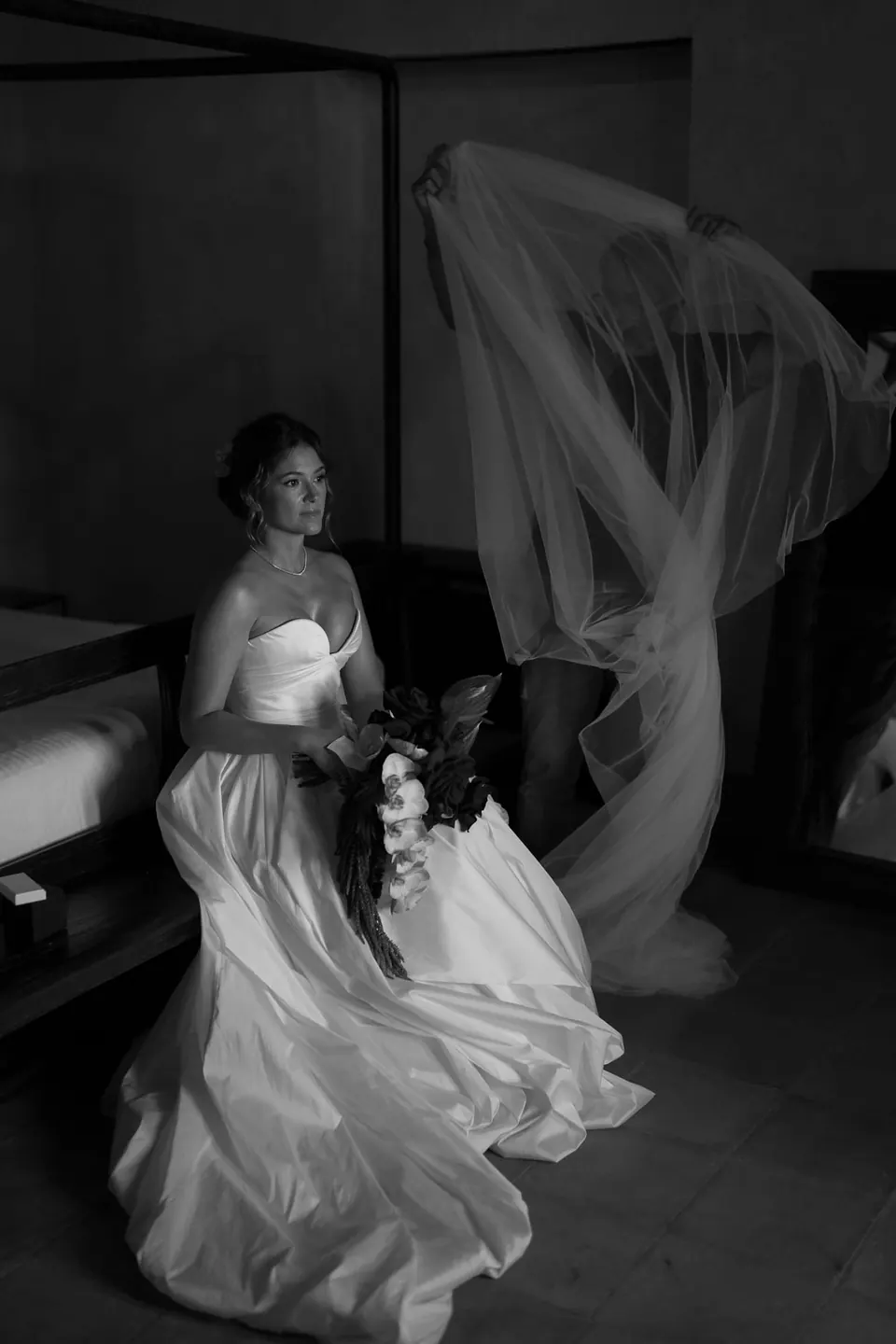 Black and white photo of the bride on the bed as her veil flies up behind her.