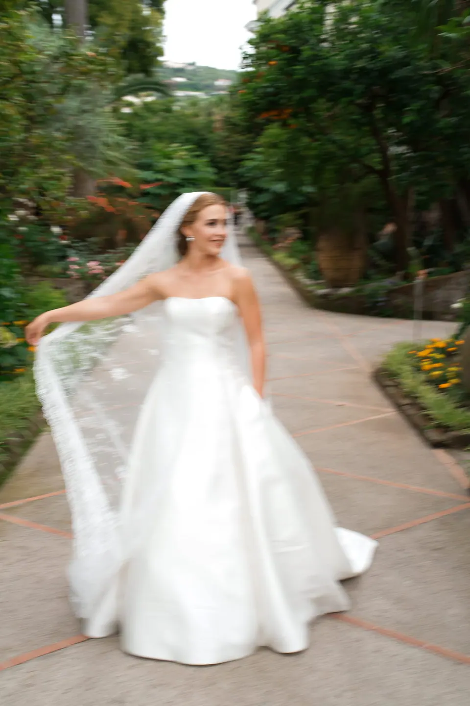 Bride walking down the garden path of La Cocumella, her veil in her hand.