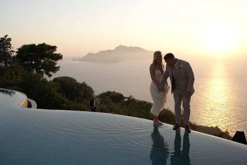 Bride and groom by the infinity pool of Relais Blu at sunset, Capri on the horizon.