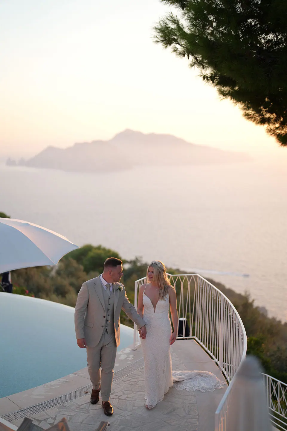 Bride and groom walking by the pool with Capri on the horizon at sunset
