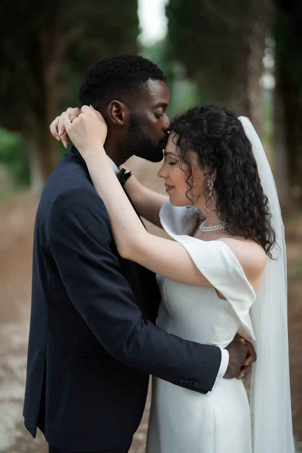 Bride and groom in a tight embrace, foreheads touching and eyes closed, intimate romantic portrait beneath the trees at the Italian villa.