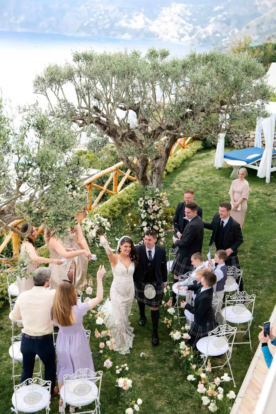 Newlyweds walking back up the aisle among guests on the lawn of Villa Milù, seen from above.