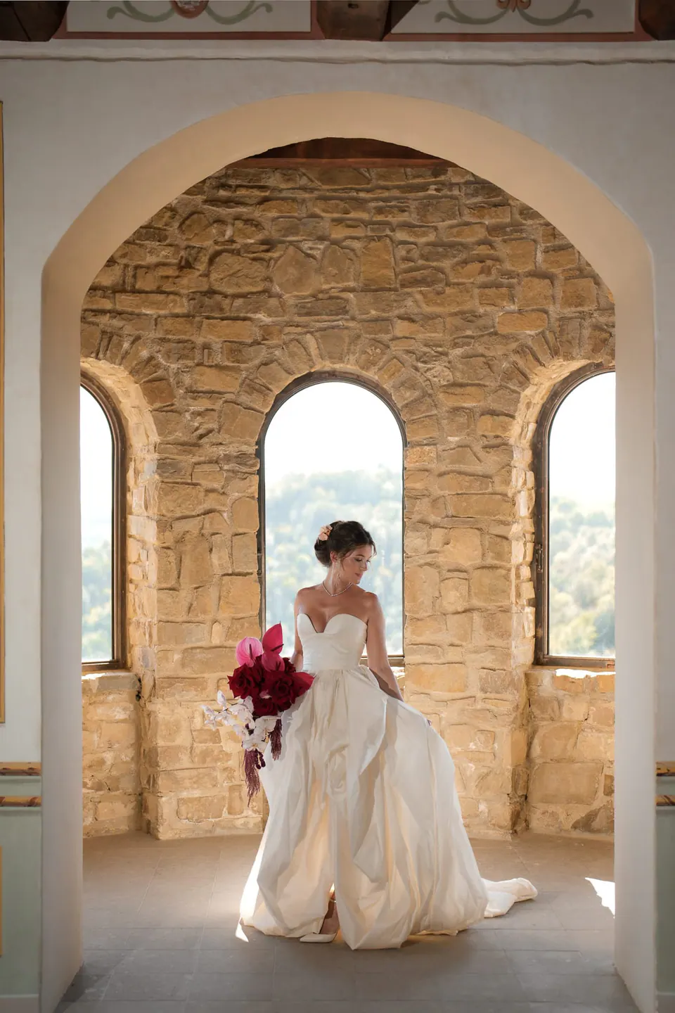 Bride seated in an arched stone window with three openings over the hills.