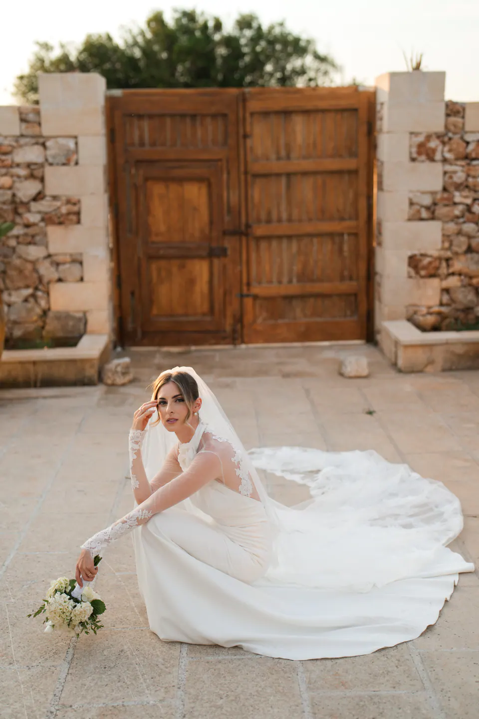 The bride crouching on the stone paving of Tenuta Sant'Elia, her train fanned out around her.